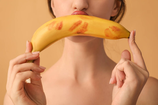 Mujer joven sosteniendo plátano con marcas de beso lápiz labial sobre fondo beige, primer plano. Concepto de sexo - Foto, Imagen
