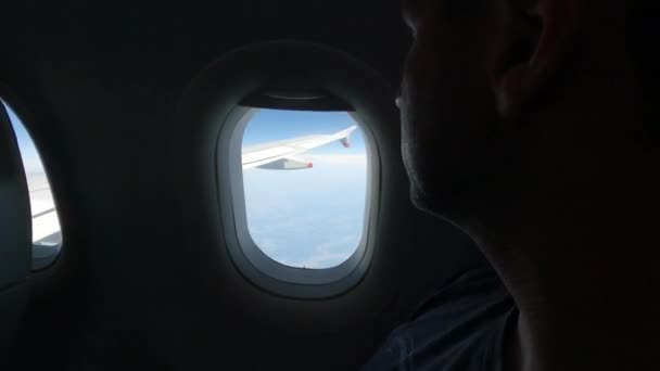 CERRAR: Pasajero macho mirando por la ventana del avión durante el vuelo. Un joven viajero turístico disfruta de hermosas vistas de las nubes y el paisaje muy por debajo mientras vuela por encima de Europa. - Metraje, vídeo