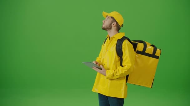Green Screen Young Food Delivery Person in gelber Uniform und mit einem Thermo-Rucksack und Smartphone, um die Bestellung zu überprüfen. Kurier auf dem Weg zum Kunden. Zurück zur Ansicht - Filmmaterial, Video