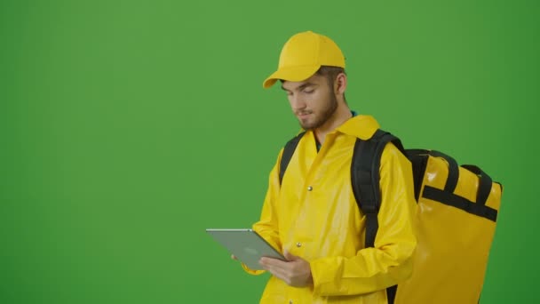 Zelená obrazovka Young Food Delivery Person ve žluté uniformě a s tepelným batohem a pomocí chytrého telefonu na kontrolu objednávky. Kurýr na cestě k doručení objednávky klientovi. Zadní pohled - Záběry, video