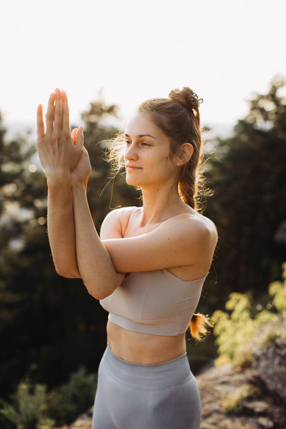 Fit young woman practices yoga on the rocks against the background of the pine forest. A beautiful girl meditates and does breathing exercises in the mountains. - Photo, Image