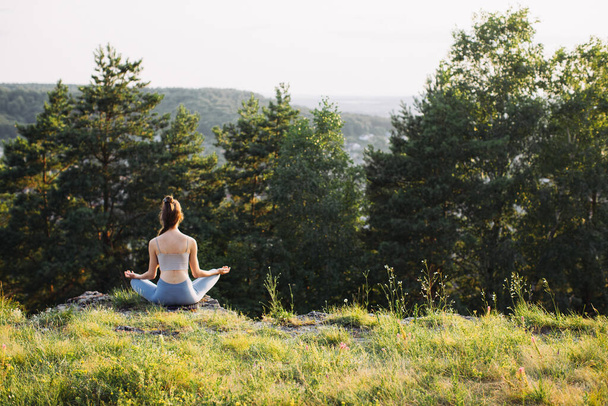 Achteraanzicht mooie jonge vrouw oefenen yoga in lotus poseren op rots in de zomer bos buiten. - Foto, afbeelding