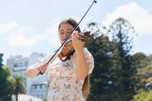 Ritratto in vita di una giovane donna felice venezuelana, immigrata in Argentina, vestita, sorridente e in piedi che suona il violino nel parco di Buenos Aires. copia spazio - Foto, immagini