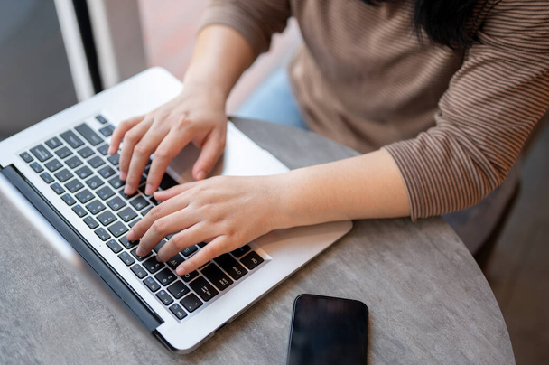Uma foto de close-up de uma mulher em roupas casuais trabalhando em seu computador portátil em um café, digitando no teclado do laptop, respondendo a e-mails ou navegando na internet. conceitos de pessoas e tecnologia - Foto, Imagem