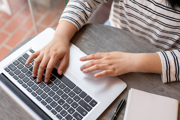 Um close-up de uma mulher em roupas casuais trabalhando em seu computador portátil, digitando no teclado enquanto trabalhava remotamente em um espaço de co-trabalho de café na cidade. - Foto, Imagem