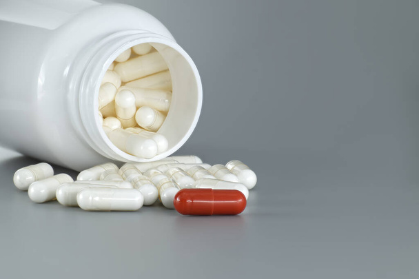 Gezondheidsgerelateerde scène met een witte fles gevuld met capsules die een intrigerende kleurencombinatie hebben van rood en wit kleurenschema, vaak geassocieerd met geneeskunde en apotheek - Foto, afbeelding