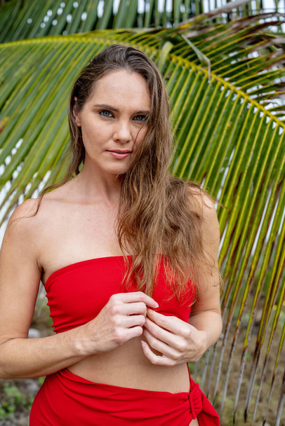 Göz kamaştırıcı esmer, canlı kırmızı bir elbise içinde ışıl ışıl, Karayip kıyılarını zarafetle süslüyor, tropik cennetin ortasında güzelliği somutlaştırıyor. - Fotoğraf, Görsel
