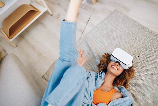 Virtuální realita zábava: Usmívající se žena těší futuristické herní zážitek doma s VR brýle na pohovce - Fotografie, Obrázek