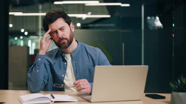 Stressed businessman sitting by table with computer and daybook and touching forehead with closed eyes. Hardworking startup runner trying meeting deadlines for making profitable deals with clients. - Footage, Video