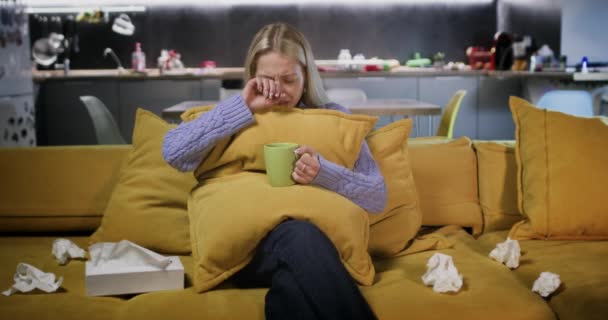 Vrouw huilt omhelzend kussen met kopje thee in handen. Lady kijkt soap opera reageren emotioneel op plot van film vegen tranen met weefsels - Video