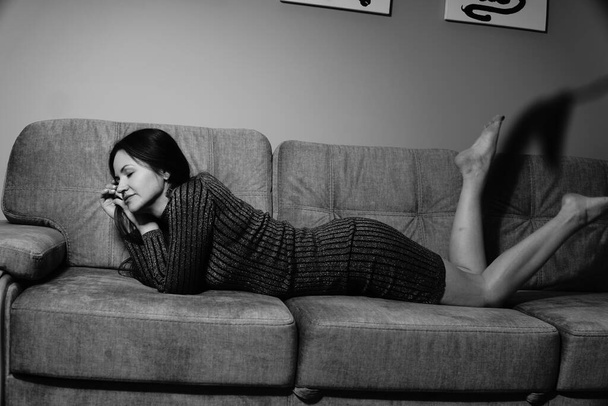 Schwarz-Weiß-Foto einer netten Frau in einem gestreiften kurzen Kleid, die auf dem Sofa im Zimmer liegt - Foto, Bild