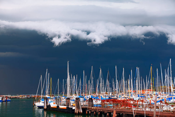 Бушующие облака, нависающие над роскошными яхтами в гавани. Яхты и лодки на пристани в бурный день - Фото, изображение