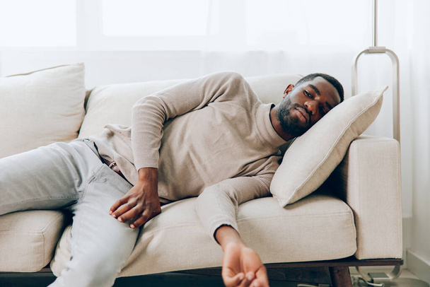 Uomo afroamericano rilassato seduto su un comodo divano nel suo salotto moderno, godendo di un fine settimana a casa con un grande sorriso sul suo viso, è felice di guardare qualcosa online, con un computer portatile in mano - Foto, immagini