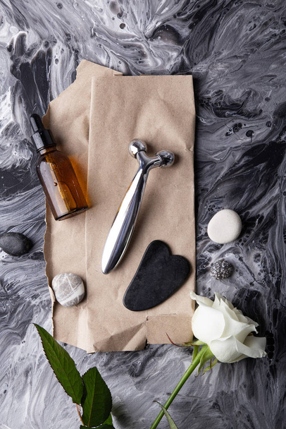 Elegant white rose with massage roller, serum, gua sha and organic skincare. Modern facial care tools with rose and essential oil for beauty routine. - Photo, Image