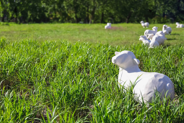 White, life-sized sheep sculptures rest in a lush green meadow - Photo, Image