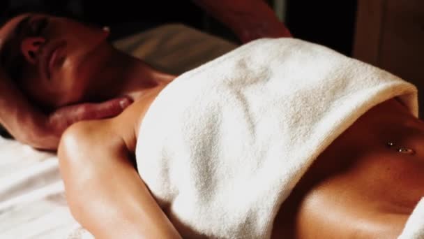 Mooie jonge vrouw geniet van massage in spa salon. Ontspannen brunette meisje liggend op massage bed met gesloten ogen tijdens de spa behandeling. Schoonheidsbehandeling, huidverzorging, welzijn.4k - Video