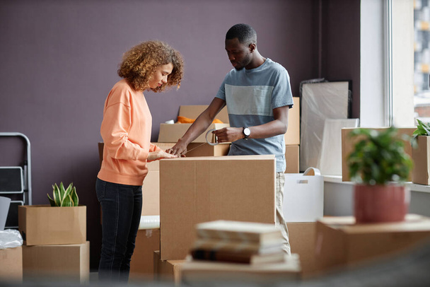 Fiatal pár csomagolás dobozok együtt ragasztószalag költözés közben egy új házba - Fotó, kép