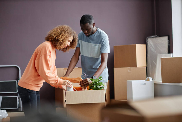 Jeune couple multiethnique emballant des choses dans des boîtes en carton pour déménager dans une nouvelle maison - Photo, image