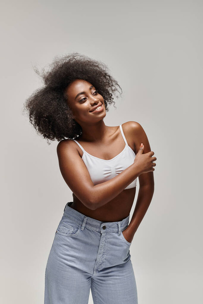 Eine schöne junge Afroamerikanerin mit lockigem Haar posiert selbstbewusst für ein Foto im Studio. - Foto, Bild