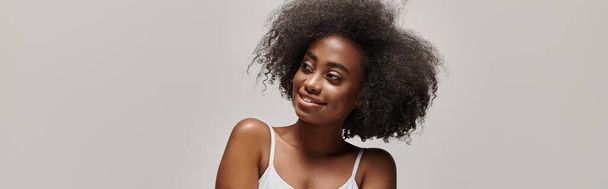 Μια όμορφη νεαρή Αφροαμερικανή με σγουρά μαλλιά που ποζάρει σε στούντιο.. - Φωτογραφία, εικόνα