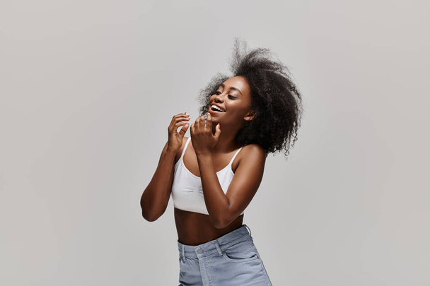A stunning African American woman with curly hair poses elegantly in a white top and denim skirt, exuding grace and style. - Photo, Image