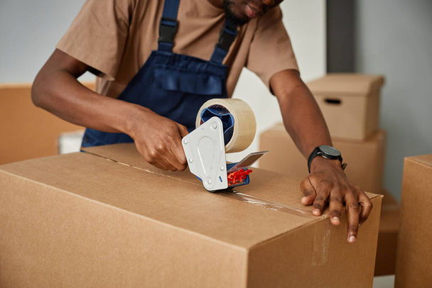 Gros plan du travailleur afro-américain dans des boîtes d'emballage uniformes avec du ruban adhésif - Photo, image