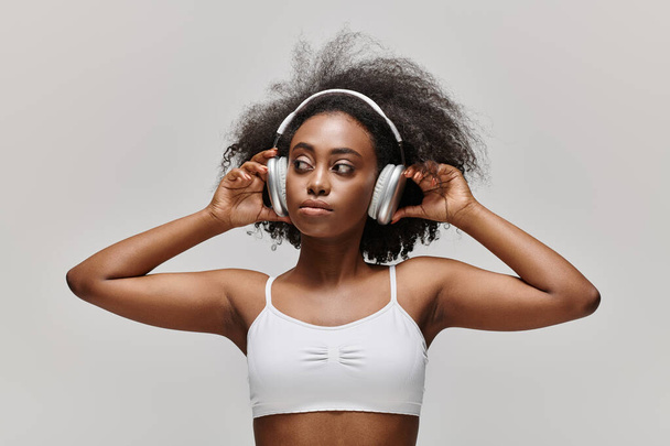 カーリーヘアの若いアフリカ系アメリカ人女性がヘッドフォンで音楽を聴く. - 写真・画像