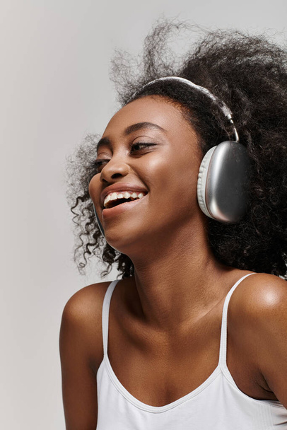 Une femme afro-américaine rayonnante aux cheveux bouclés, souriante en écoutant de la musique à travers des écouteurs. - Photo, image