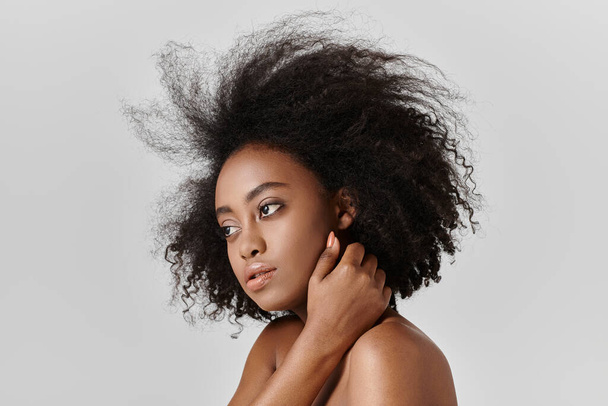 Kaunis nuori afroamerikkalainen nainen, jolla on kiharat hiukset, aiheuttaa luottavaisesti kuvan studiossa.. - Valokuva, kuva