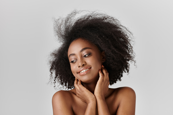 Una hermosa joven afroamericana con el pelo rizado peinado en un afro golpea una pose segura en un entorno de estudio. - Foto, imagen
