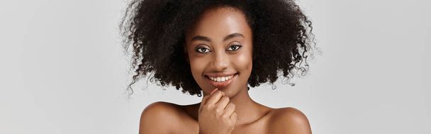 Stylowa młoda Afroamerykanka z kręconą fryzurą afro uderza w pozę w studio. - Zdjęcie, obraz