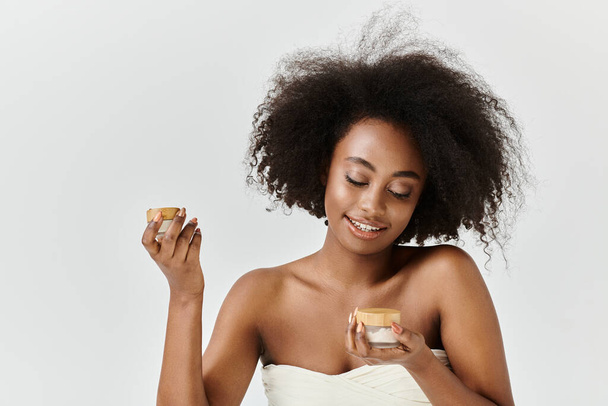 A stunning young African American woman, wrapped in a towel, holds a jar with cream - Photo, Image