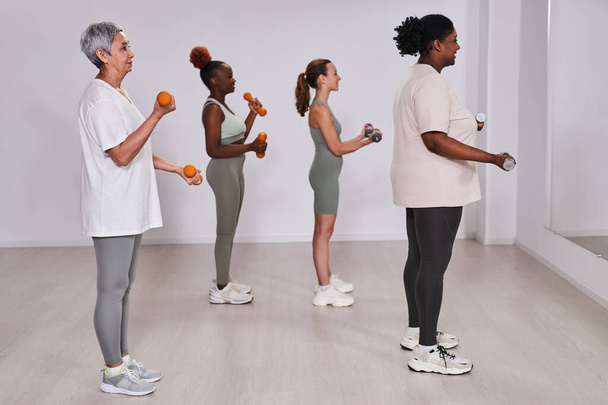 Gruppe von Menschen, die vor dem Spiegel stehen und im Fitnessstudio mit Hanteln trainieren - Foto, Bild