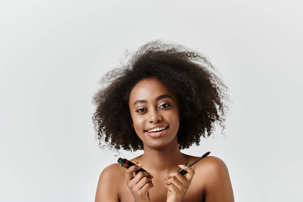Uma mulher afro-americana sorridente com um rímel de aplicação afro em um estúdio, exalando alegria e criatividade. - Foto, Imagem