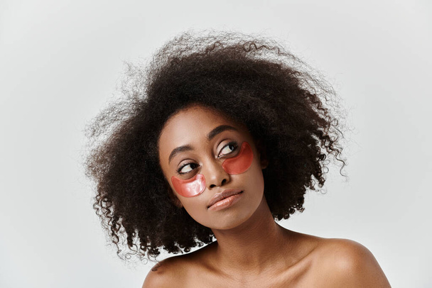 赤い目のパッチを着たカーリーヘアの印象的なアフリカ系アメリカ人女性が,スタジオでユニークなスキンケアコンセプトを披露. - 写真・画像