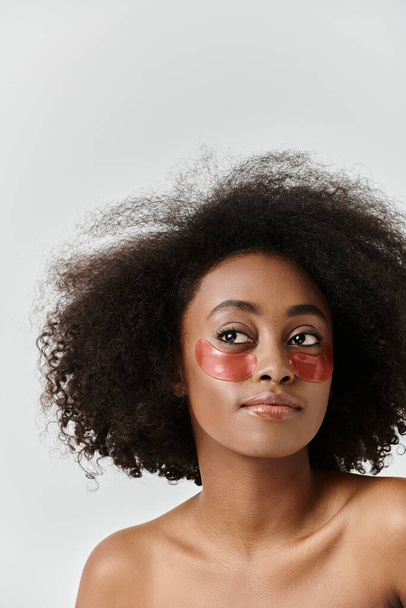 Eine auffallende Afroamerikanerin mit lockigem Haar trägt eine leuchtend rote Augenklappe und präsentiert ein einzigartiges und kühnes Hautpflegekonzept. - Foto, Bild