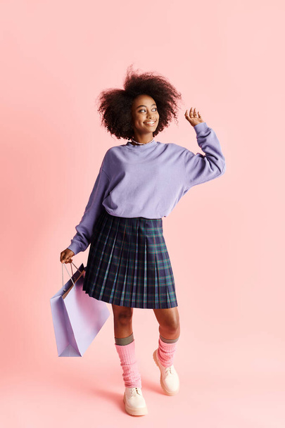 カーリーヘアのファッショナブルなアフリカ系アメリカ人女性は,紫色のセーターと平らなスカートで買い物袋を保持しています. - 写真・画像