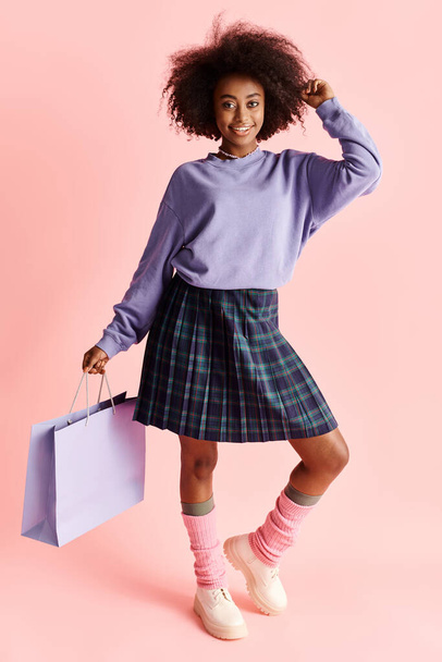 Afrikai amerikai lány göndör hajjal, szoknyát és zoknit visel, egy bevásárlószatyrot tart egy divatos stúdióban. - Fotó, kép
