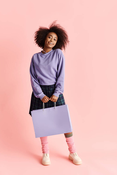Eine schöne junge Afroamerikanerin mit lockigem Haar lächelt, während sie in einem Studio eine Einkaufstasche hält. - Foto, Bild