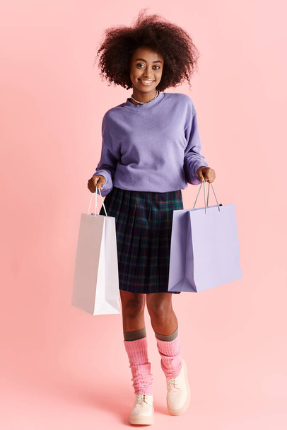 Uma bela jovem afro-americana com cabelo encaracolado segurando sacos de compras e sorrindo em um ambiente de estúdio. - Foto, Imagem