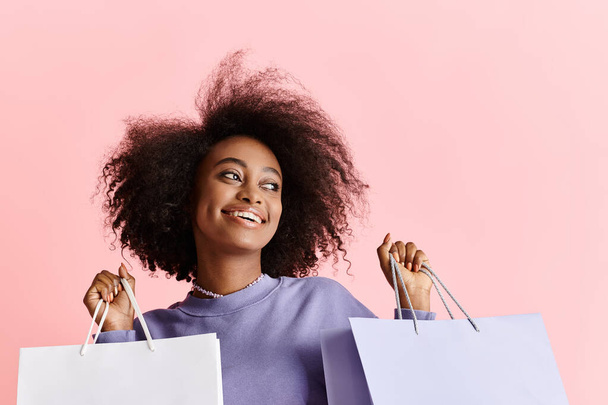 Egy fiatal afro-amerikai nő göndör hajjal mosolyog, miközben bevásárlószatyrokat tart a stúdióban.. - Fotó, kép