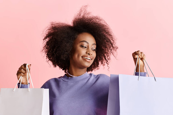 Eine schöne junge Afroamerikanerin mit lockigem Haar steht lächelnd und hält Einkaufstüten in der Hand.. - Foto, Bild