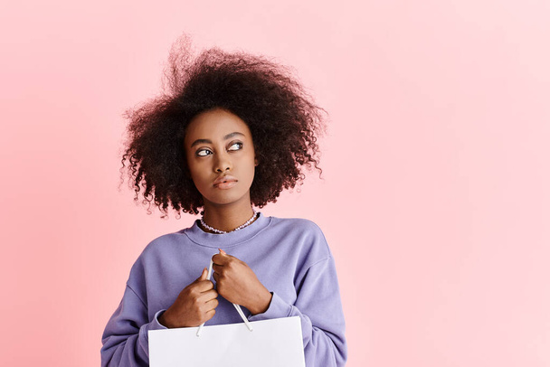 Stilvolle junge Afroamerikanerin mit lockigem Haar hält eine Einkaufstasche in der Hand und präsentiert Mode und Glamour. - Foto, Bild
