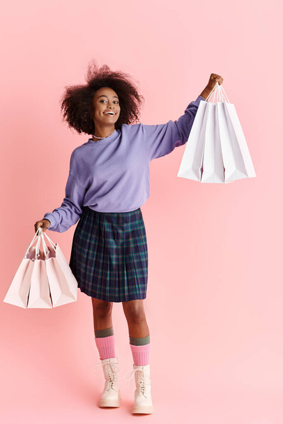 Kıvırcık saçlı, mor kazaklı ve ekose etekli genç Afro-Amerikan kadın, alışveriş torbaları tutuyor.. - Fotoğraf, Görsel