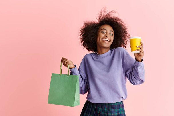 Gyönyörű afro-amerikai nő göndör haj kezében egy csésze kávét és egy papírzacskót, élvezi a reggeli bevásárlás ámokfutás. - Fotó, kép