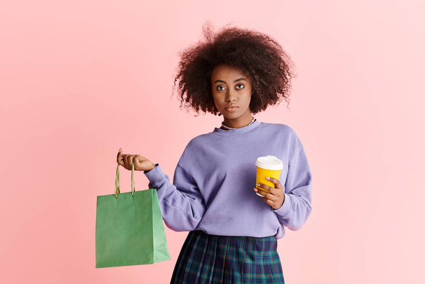 Une femme afro-américaine chic aux cheveux bouclés tient une tasse de café et un sac en papier. - Photo, image