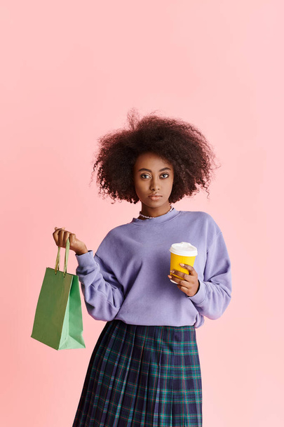 Uma mulher afro-americana de cabelos encaracolados sorri enquanto segura uma xícara de café e um saco de papel. - Foto, Imagem