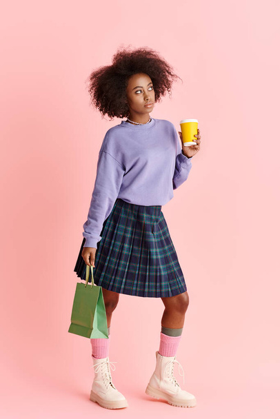 Elegancka Afroamerykanka z kręconymi włosami, w modnej spódnicy, pije filiżankę kawy. - Zdjęcie, obraz