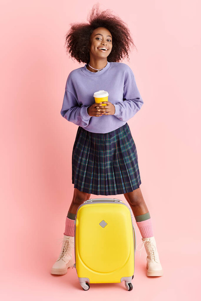 Genç bir Afrikalı Amerikalı kadın elinde bavuluyla şık bir stüdyoda elinde bir fincan kahve tutuyor.. - Fotoğraf, Görsel
