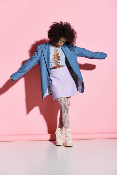 Una joven y elegante mujer afroamericana con el pelo rizado se para con confianza frente a una vibrante pared rosa en un entorno de estudio de moda. - Foto, Imagen